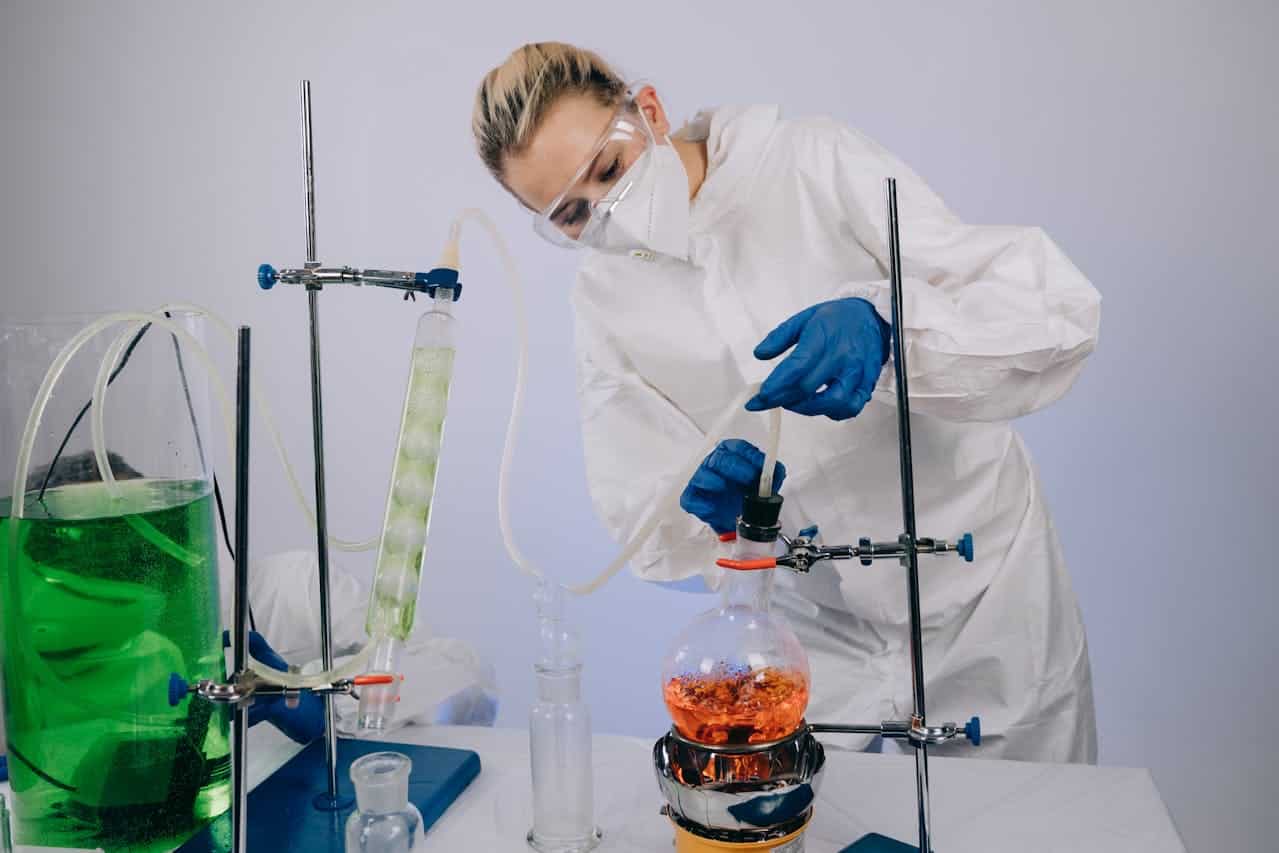 Naukowiec badający zawartość kolby kulistej ustawionej na statywie laboratoryjnym.